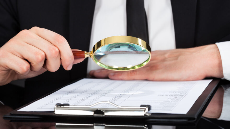 Businessman Analyzing Document With Magnifying Glass At Desk