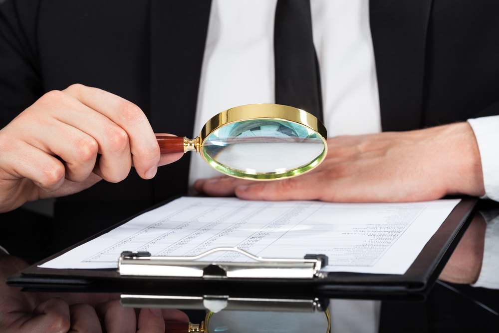 Businessman Analyzing Document With Magnifying Glass At Desk